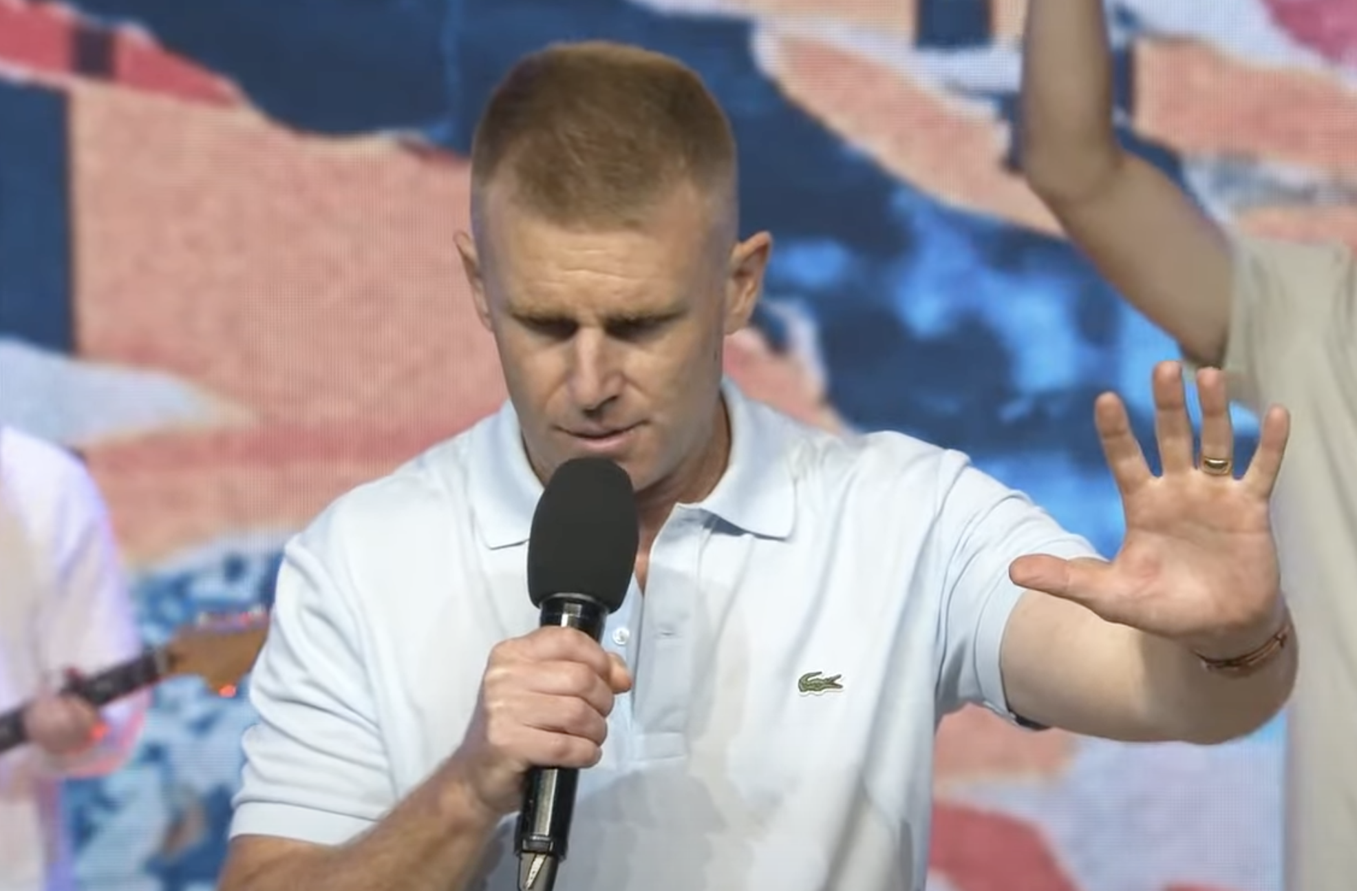 John Cameron gripping a mic with his praying hand up